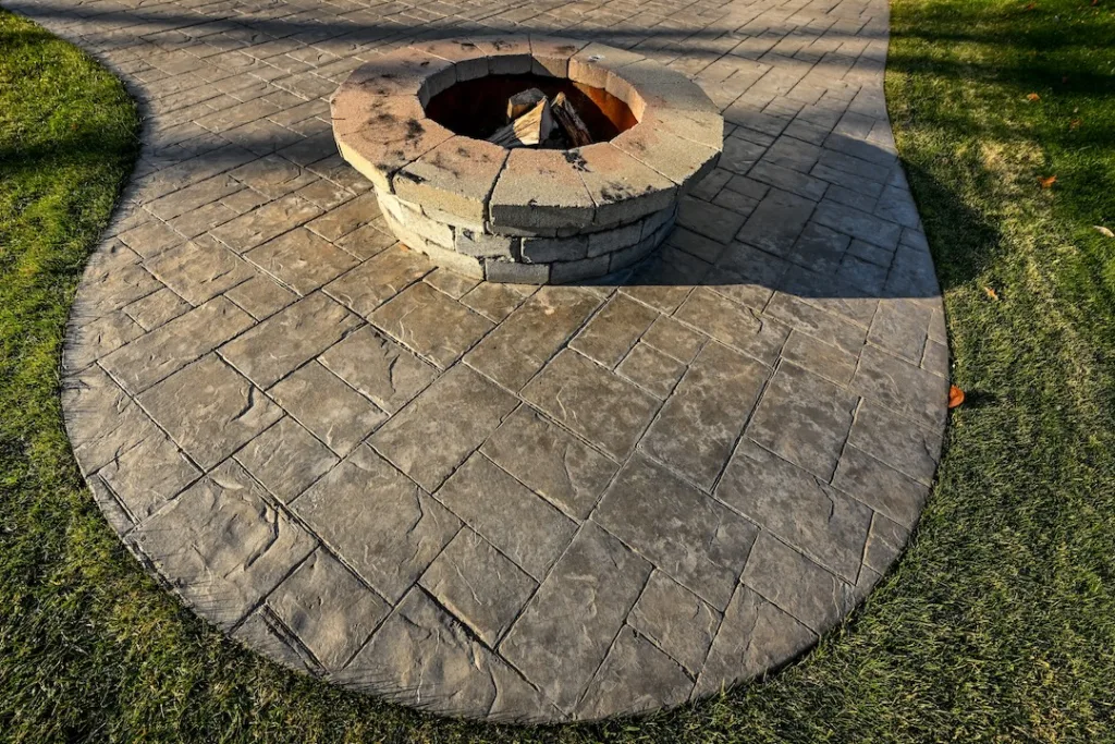 round stone fire pit on stamped concrete patio in grass yard